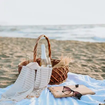 Two glasses of champagne and sunglasses in a picnic basket against the beach and the sea